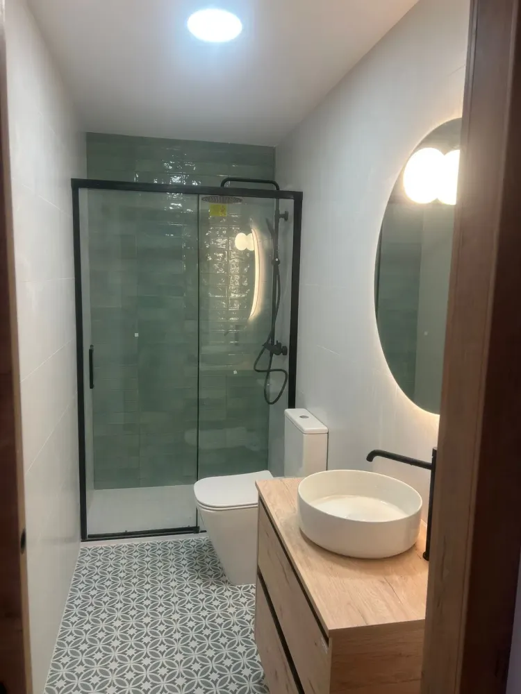 Baño reformado en Santiago con ducha de azulejo verde, mampara negra y suelo hidráulico