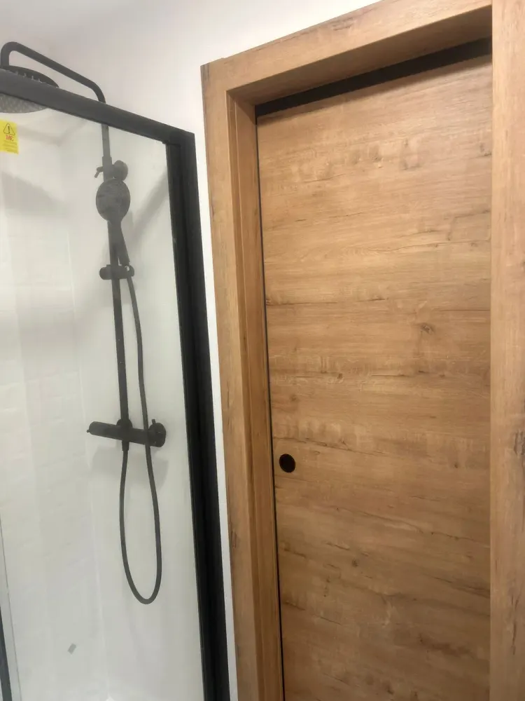 Detalle de ducha con columna negra y puerta de madera en reforma de baño en Santiago