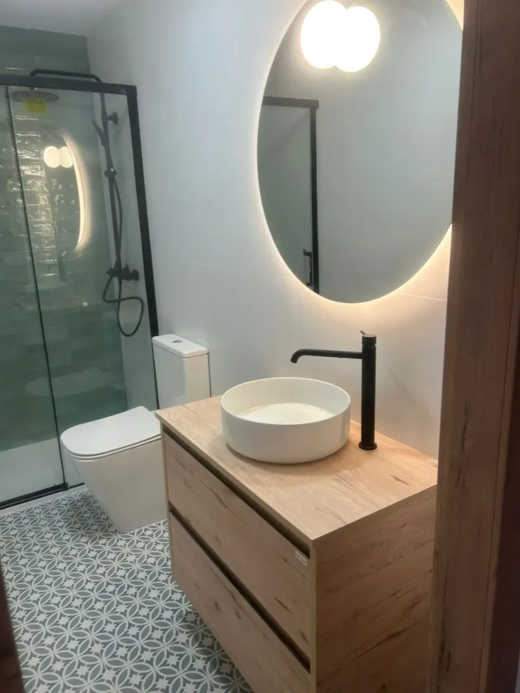Baño reformado en Santiago con espejo redondo retroiluminado y mampara negra